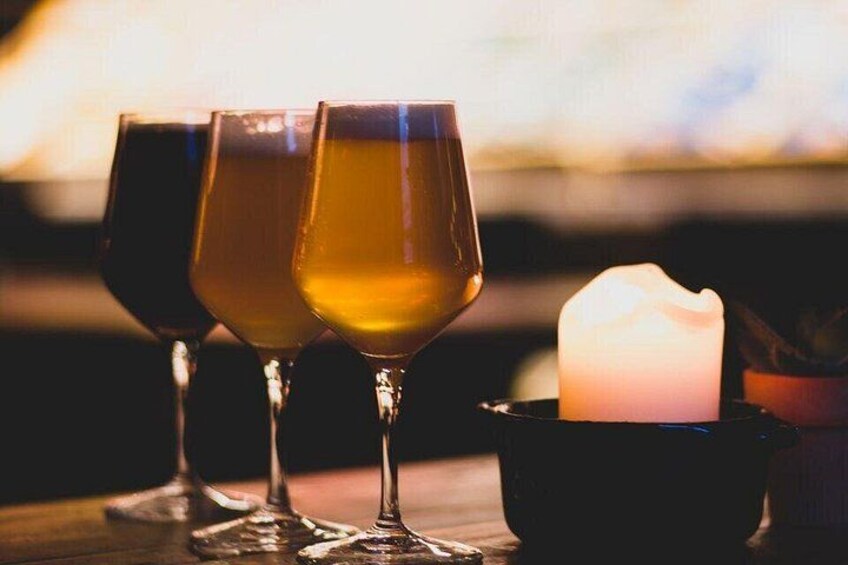 Three glasses of amber liquid, a lit candle, and a dark bowl on a wooden surface. 1