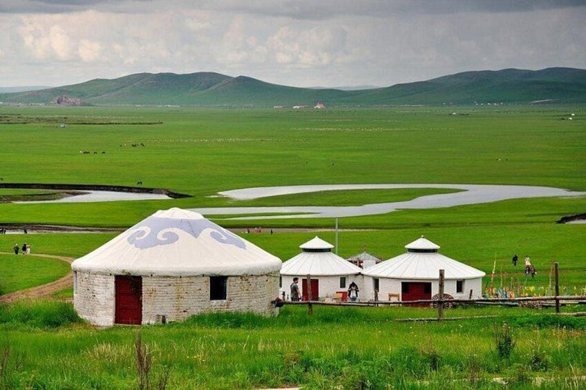 A yurt with a red door, a white yurt with a blue design, and a white yurt with a red door in a grassy field with mountains in the background. 5