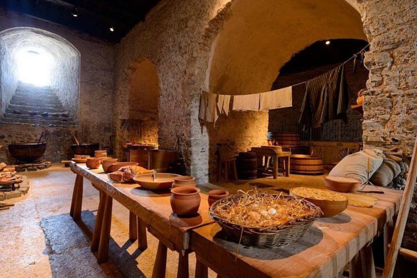 A historical kitchen with stone walls, wooden tables, and various cooking utensils. 4