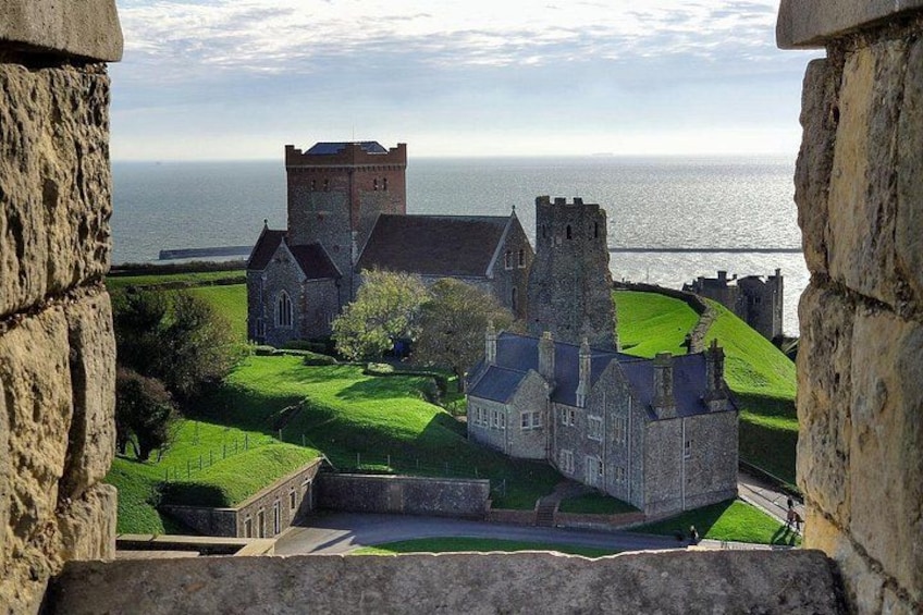 A historic stone building with a tower, surrounded by green lawns and a body of water in the background. 3