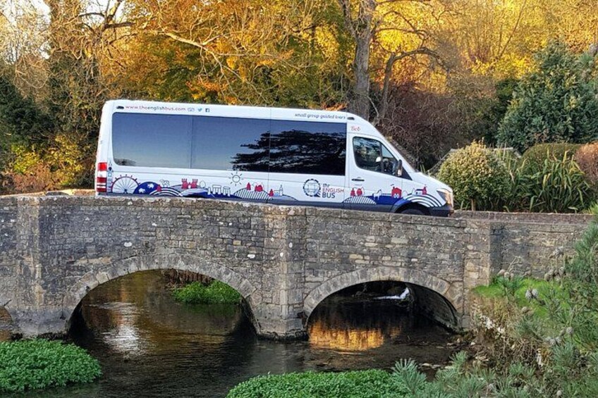 Een witte bus met kleurrijke ontwerpen geparkeerd op een stenen brug over een rivier. 2