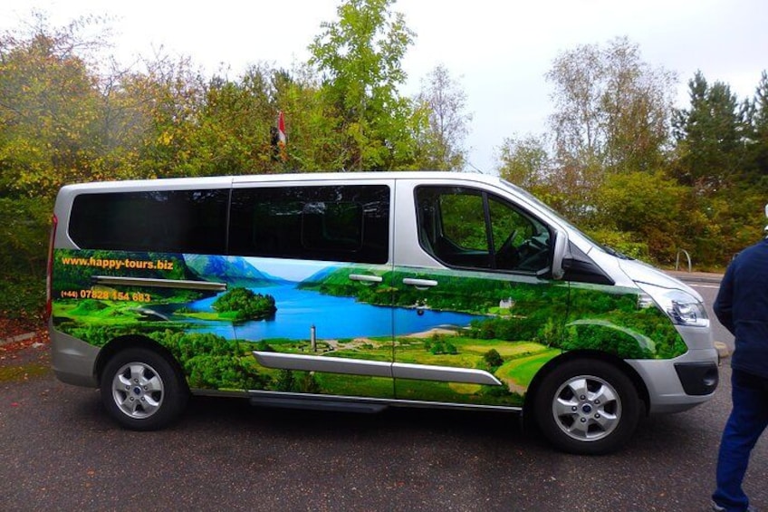 A green and white van with a scenic landscape design, parked on a road with trees in the background. 2