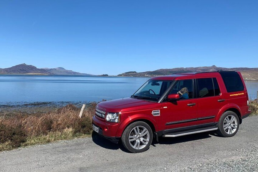 A red SUV parked by a lake with mountains in the background. 3
