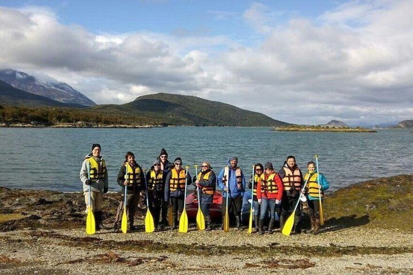A group of people standing by a lake with paddles, wearing life jackets, and a mountainous landscape in the background. 3