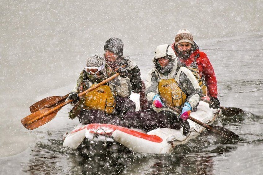 A group of people in a snow-covered inflatable raft, paddling through a snowy river. 5