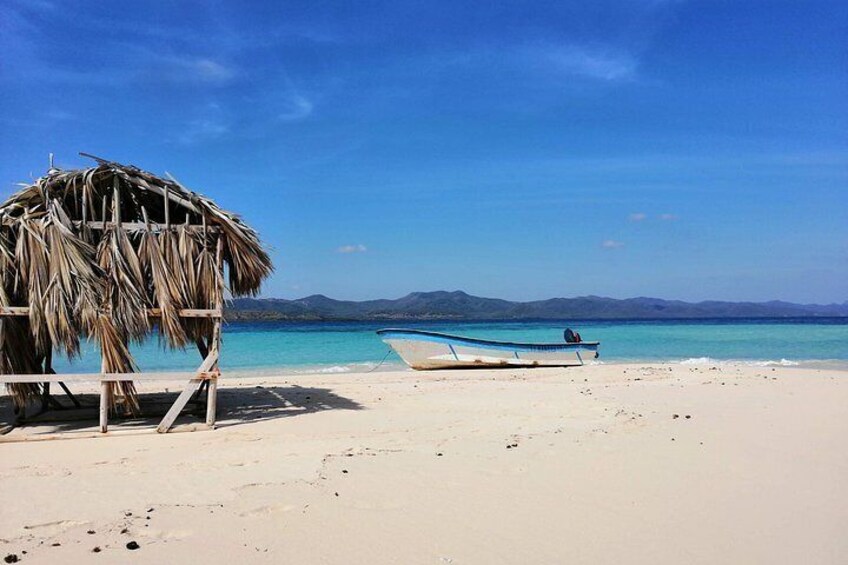 Una playa con una cabaña de techo de paja, un bote pequeño y un cielo azul despejado. 2