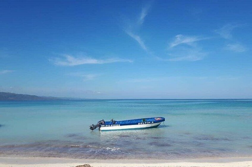 Un bote azul en una playa con agua cristalina y una costa lejana. 3