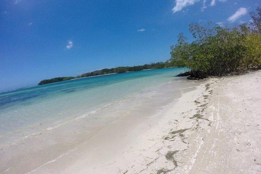 A beach with clear turquoise water, white sand, and a small island in the distance. 3