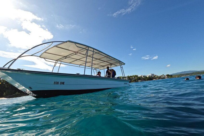 A boat named 'EGO ONE' on clear blue water with a canopy, surrounded by calm sea and distant land. 2