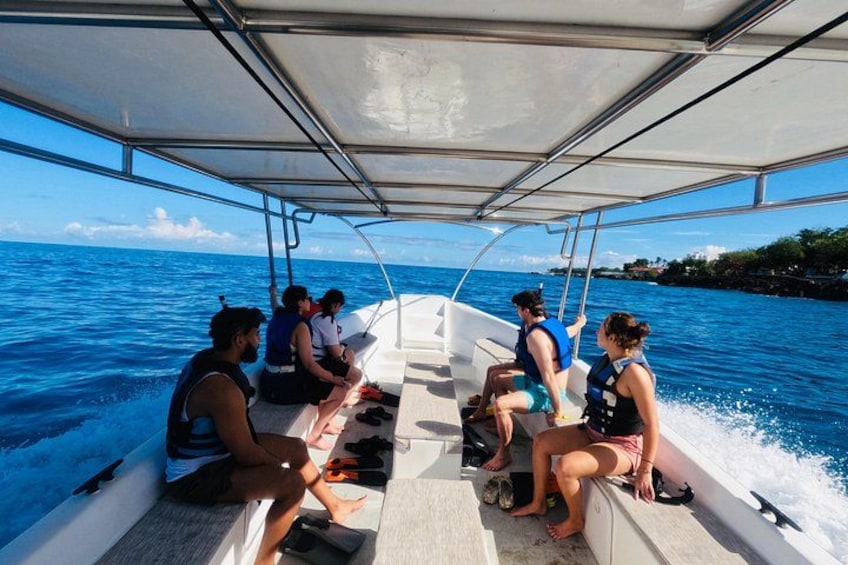 A boat with people seated under a canopy, water in the background. 1