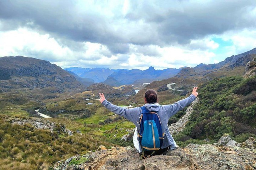 A person with arms outstretched on a rocky outcrop overlooking a valley with mountains in the distance. 3