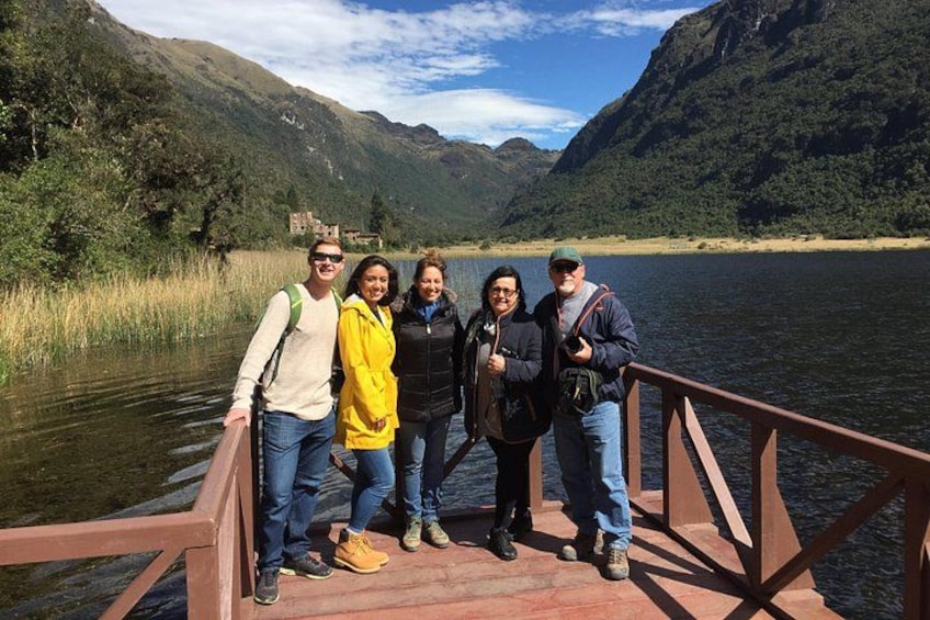Un grupo de personas en un puente de madera sobre un lago, con montañas al fondo. 3