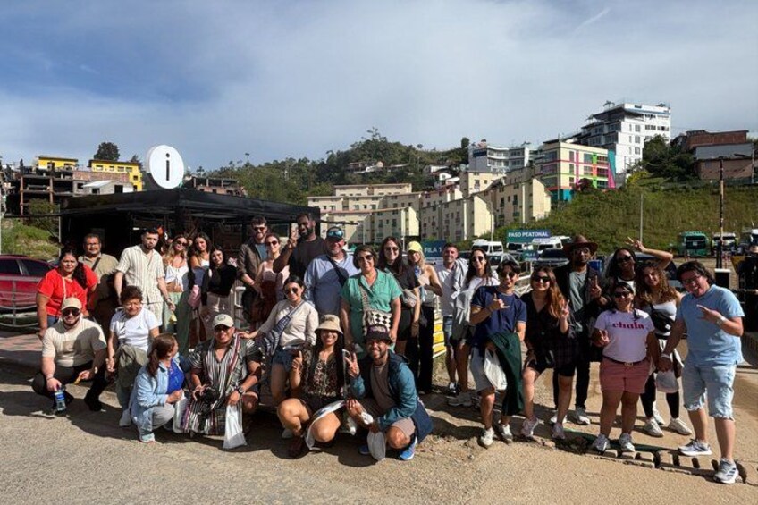A group of people gathered outdoors, some sitting and some standing, with buildings and a road in the background. 4