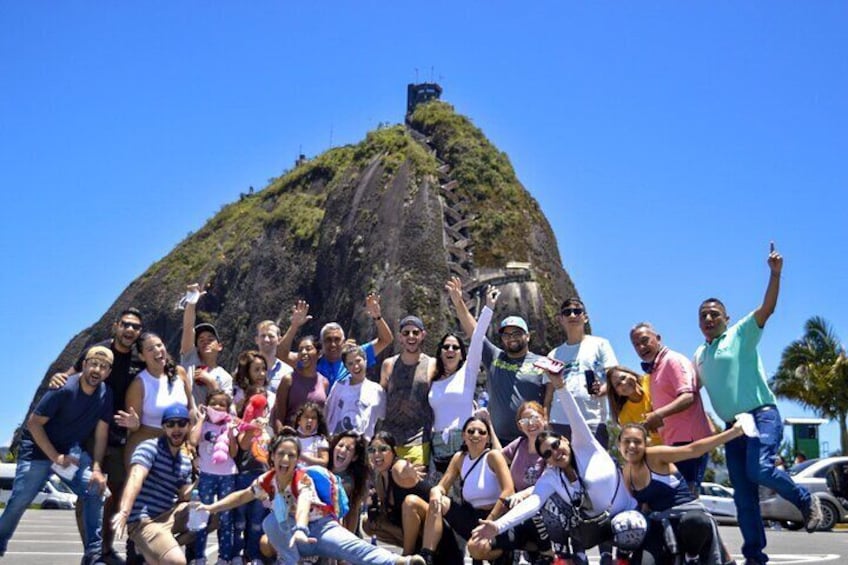 A group of people posing in front of a large, steep hill with a structure at the top. 5