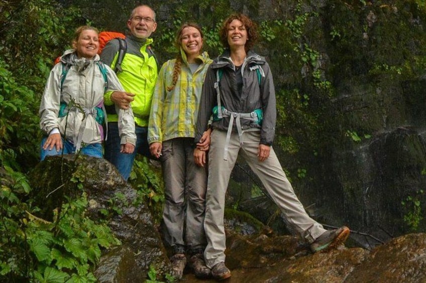 A group of people hiking in a forested area with a waterfall in the background. 4