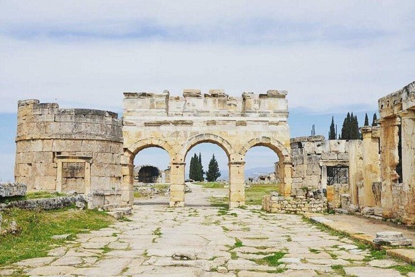 Ancient ruins with stone arches and columns, a pathway, and a distant view of trees. 3