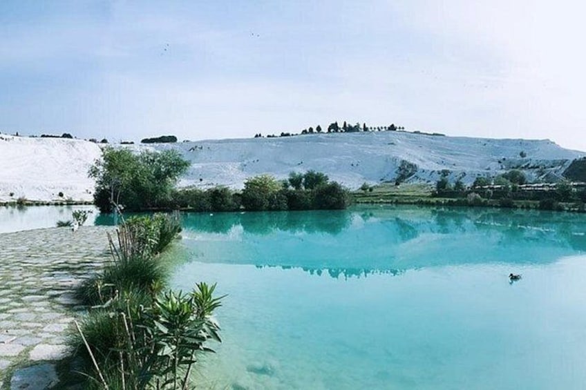 A clear blue lake with a rocky shore, surrounded by greenery and a hill in the background. 4