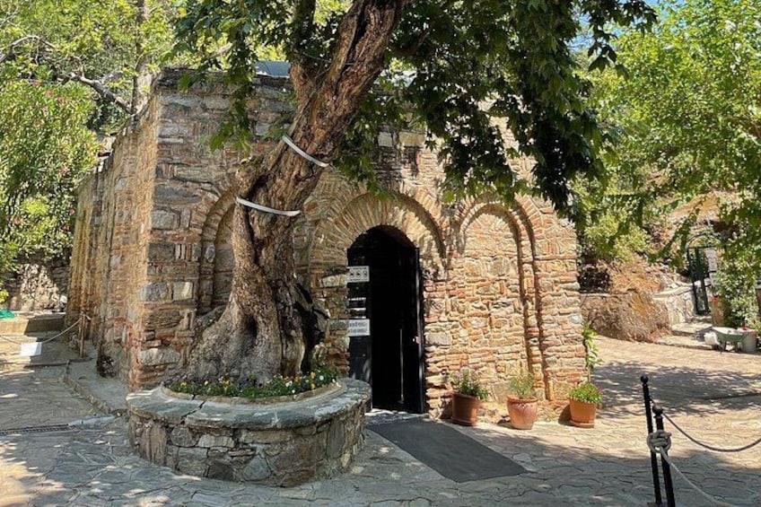 An ancient stone building with an arched entrance, surrounded by trees and potted plants. 5