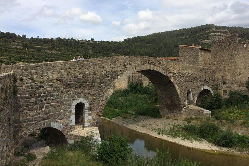 A stone bridge with arches over a river, surrounded by greenery and hills. 2