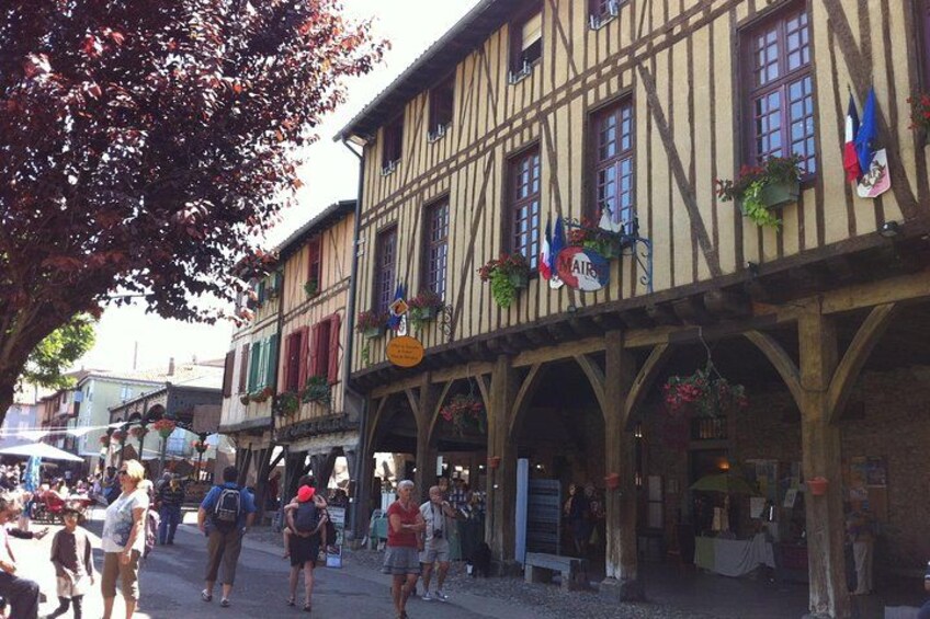 A bustling medieval-style street with half-timbered buildings, pedestrians, and outdoor seating areas. 2