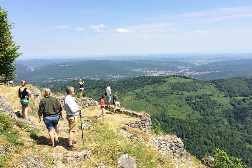 A group of people hiking on a rocky path with a view of a forested valley and distant town. 1