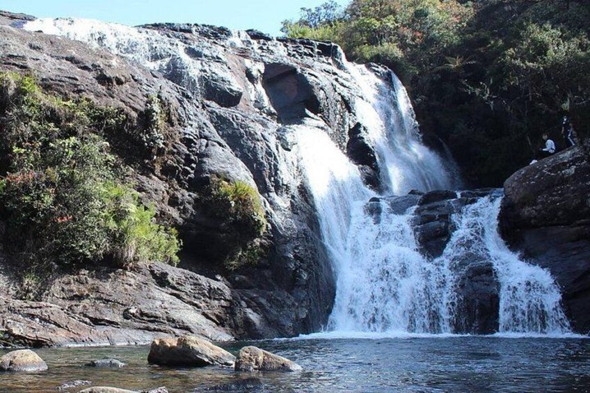A waterfall cascading over rocks into a river, surrounded by greenery. 1