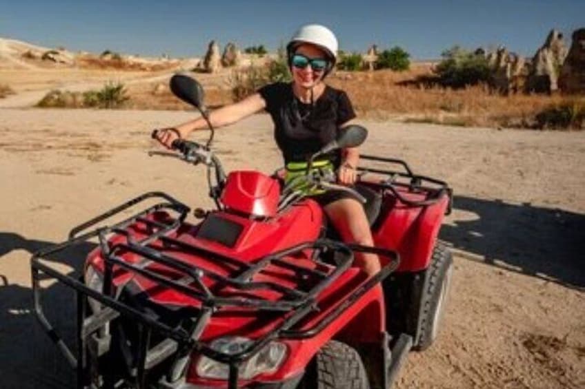 A person on a red ATV in a desert landscape with rocky formations. 5