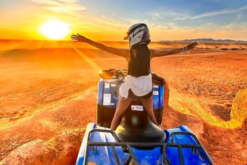 A person on a blue ATV in a desert landscape with a sunset in the background. 1
