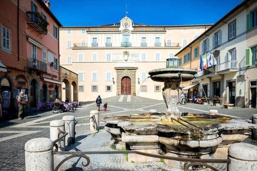A historic square with a fountain, buildings, and a clock tower. 1