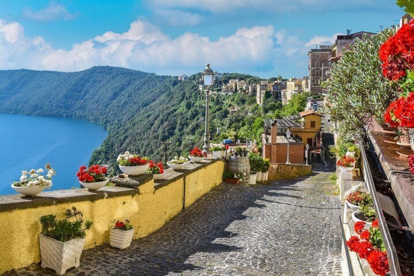 A cobblestone street with flower pots and a view of a lake and hills. 1