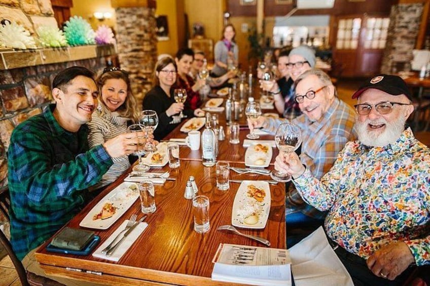 A group of people seated around a wooden table in a restaurant, holding wine glasses. 3