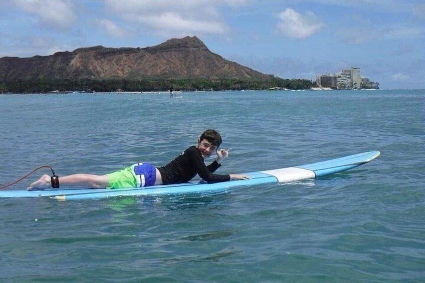 Una persona sdraiata su una tavola da surf in acque calme, con una montagna e degli edifici sullo sfondo. 3