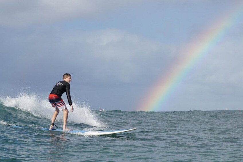 A person surfing on a wave with a rainbow in the background. 4