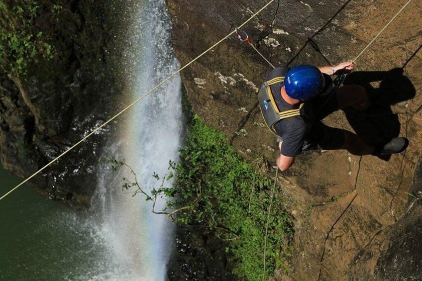 A person rappelling down a rocky cliff with a waterfall in the background. 2