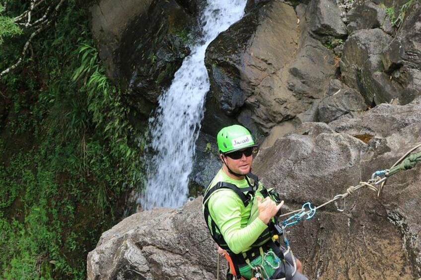 A person rappelling near a waterfall with dense foliage in the background. 3