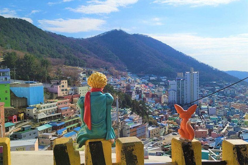 A person in a green jacket and red scarf overlooking a cityscape with mountains in the background. 4