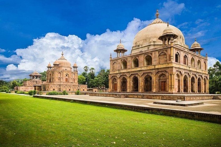 A large, historic building with domes and arches, surrounded by a well-maintained lawn and a clear sky. 2