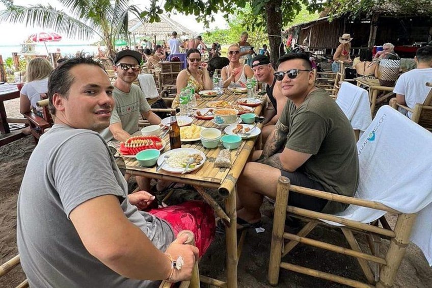 People sitting at wooden tables outdoors with food and drinks. 2