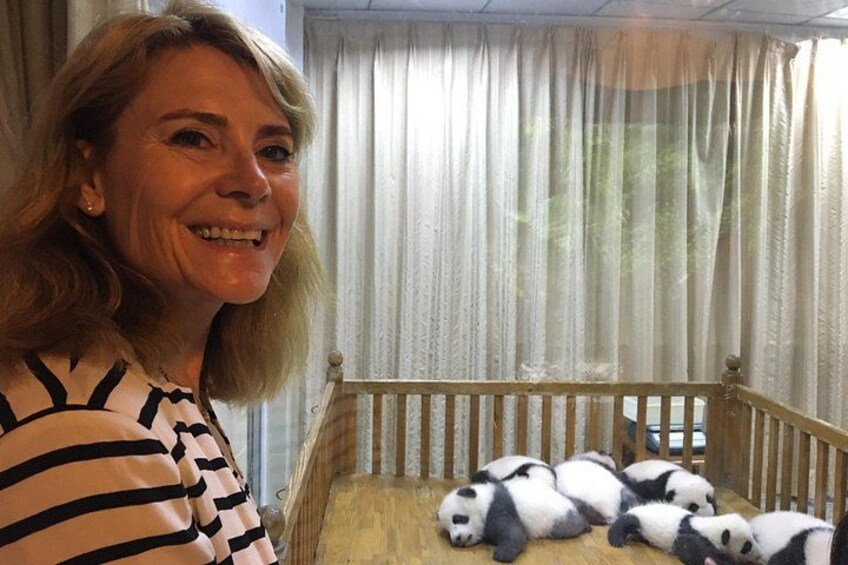 A person standing next to a wooden crib with panda cubs inside. 2