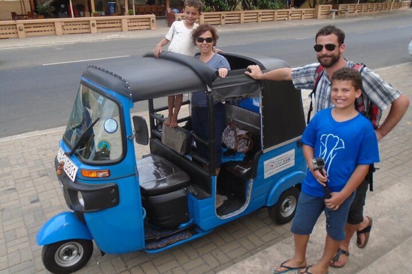 Un auto-rickshaw azul estacionado en una acera, con tres personas de pie a su lado. 2