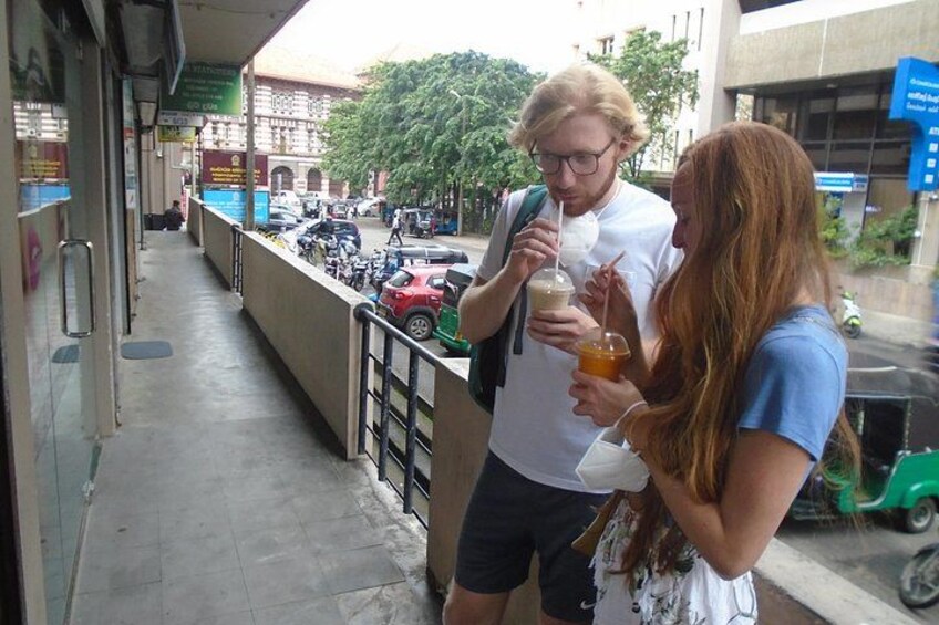 A man and a woman standing on a sidewalk, holding drinks. 2