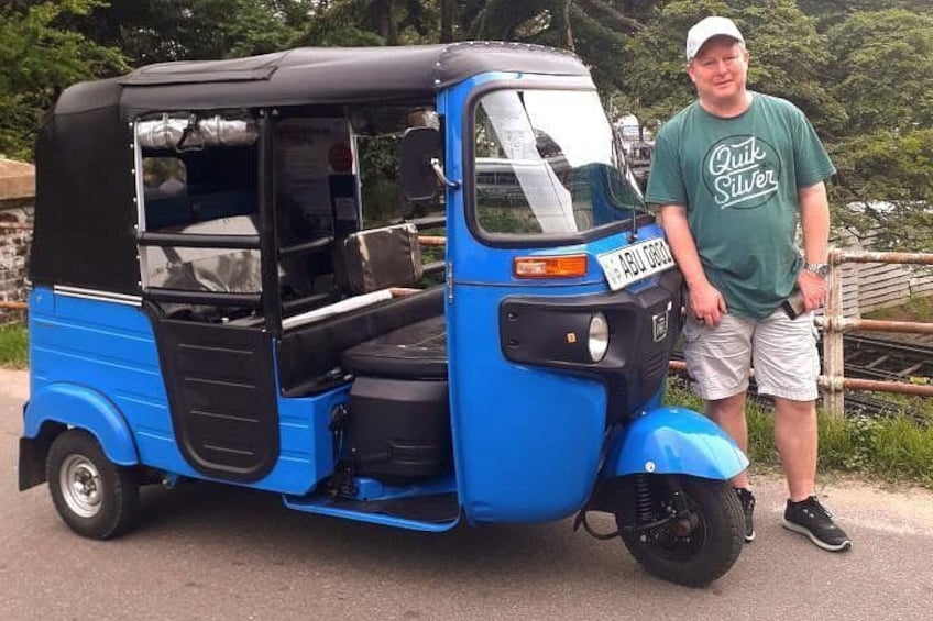 A blue auto-rickshaw parked on a road with a man standing beside it. 5