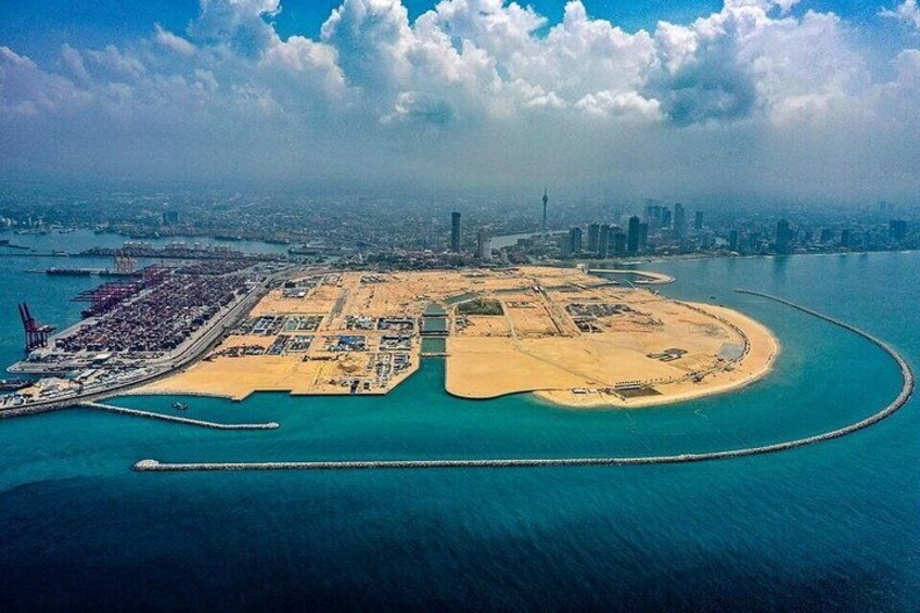 An aerial view of a coastal city with a large marina, a curved breakwater, and a dense urban skyline in the background. 5