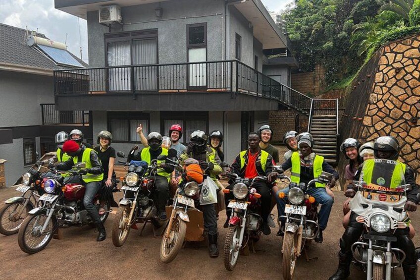 A group of people on motorcycles wearing safety vests, gathered in front of a building with a stone wall and a staircase. 4