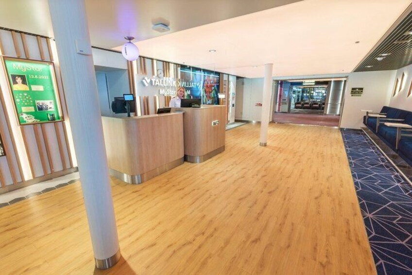 A modern hotel lobby with wooden flooring, reception desks, and a blue patterned carpet. 2