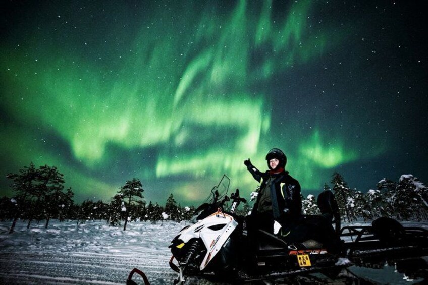 Una persona en un vehículo de nieve con la aurora boreal al fondo. 3