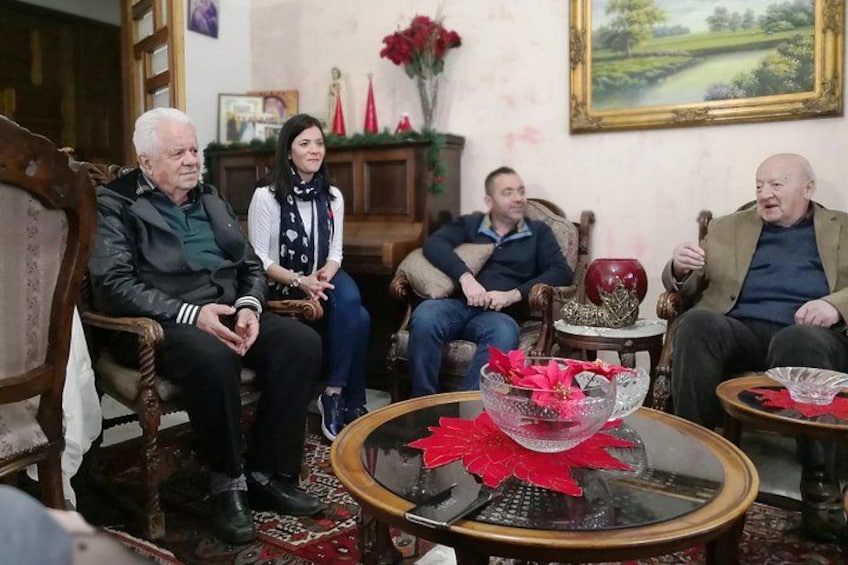 Four people seated in a room with wooden furniture and a red floral centerpiece on a glass table. 2