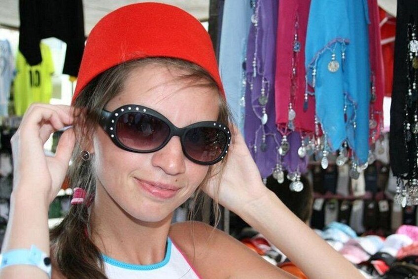 Une personne portant un chapeau rouge et des lunettes de soleil, avec en arrière-plan divers vêtements aux couleurs vives. 3