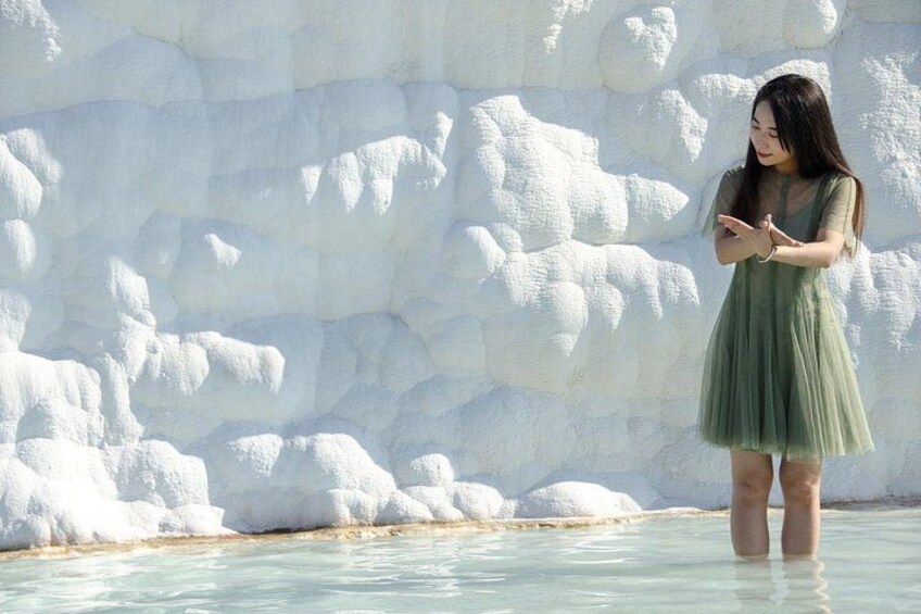 A person standing in a body of water with a large, textured rock formation in the background. 4
