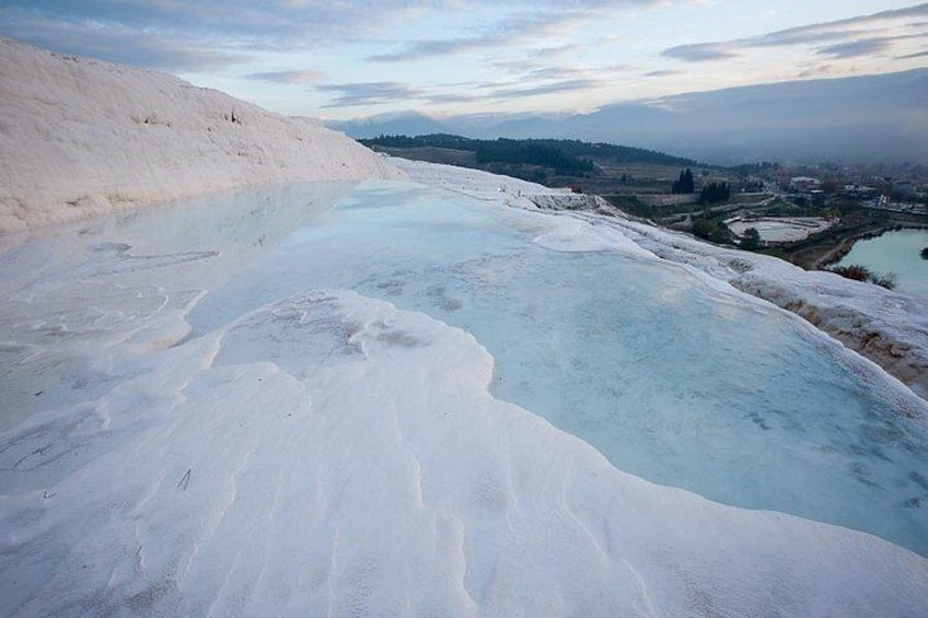 A terraced landscape with a turquoise pool, white terraces, and distant buildings. 5